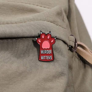 Funny Murder Mittens red cat paw enamel pin badge displayed on a canvas backpack strap