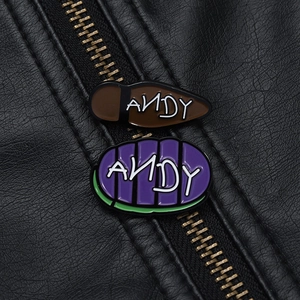 Detailed macro shot of Andy name enamel pins on black leather texture with zipper detail
