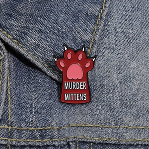 Macro shot of Murder Mittens cat paw enamel pin on a denim jacket collar