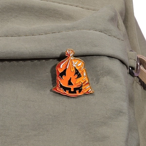 Detailed view of an orange pumpkin trash bag enamel pin on a green canvas bag