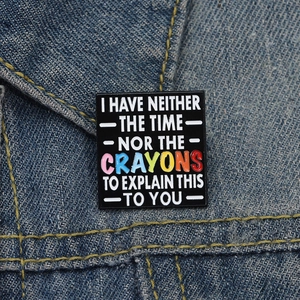 Detail of square black enamel brooch with humor text on blue denim background