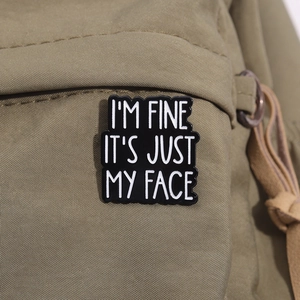 Detail of I'M FINE enamel pin on khaki canvas backpack showing the humorous quote