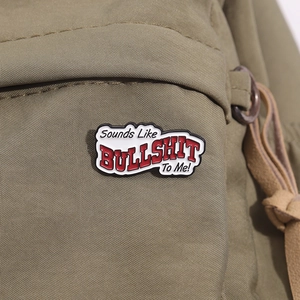 Macro detail of 'Sounds Like BULLSHIT To Me!' enamel pin on green canvas fabric
