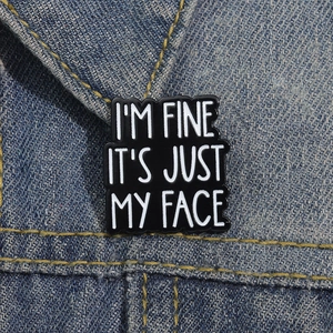 Detail of enamel pin with 'I'M FINE IT'S JUST MY FACE' quote on blue denim jacket