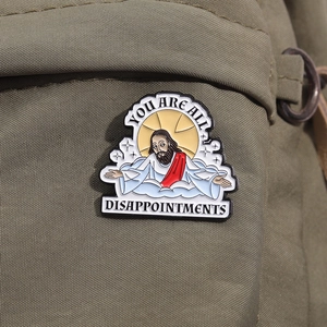 Détail macro du pin's émaillé Jésus avec texte drôle sur un sac en toile verte
