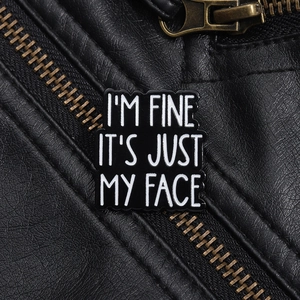 Macro detail of 'I'M FINE' enamel pin on a black leather jacket with zipper texture
