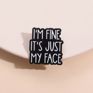 Minimalist black enamel pin with I'M FINE IT'S JUST MY FACE text on display stand