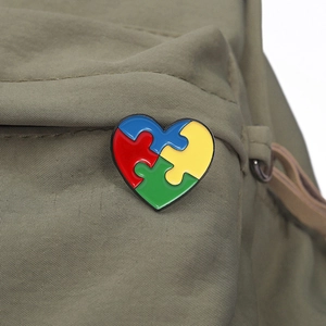 Detail of puzzle heart enamel pin for autism awareness on olive green canvas bag