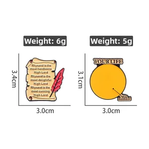 Détail de broches en émail orange avec citations littéraires et plumes gravées