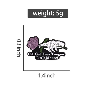 Detail of gothic enamel pin showing skeleton hand with rose and Cat Got Your Tongue text