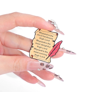 Broche en émail avec parchemin et plume rouge portant une citation de Rhysand