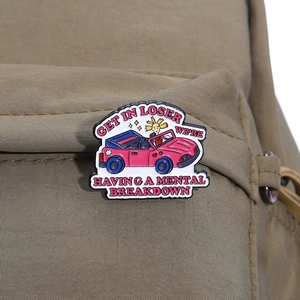 Detailed close-up of a cartoon enamel pin attached to a brown canvas backpack