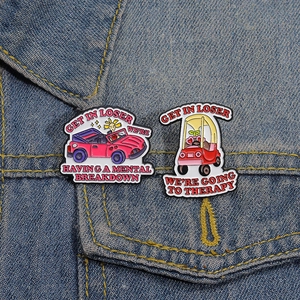 Pink and red car enamel pins with funny slogans on blue denim jacket surface
