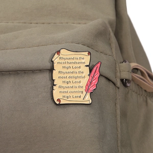 Vue détaillée d'une broche en émail en forme de parchemin avec plume rouge sur toile