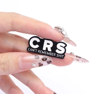 Black enamel pin with CRS text Can't Remember Shit held between fingers on white background