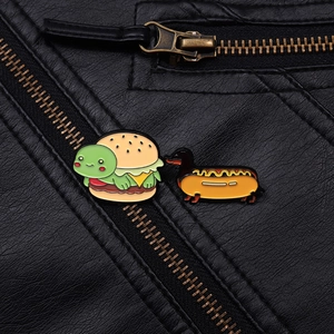Détail des broches émaillées tortue-burger et teckel-hotdog sur une veste en cuir noir