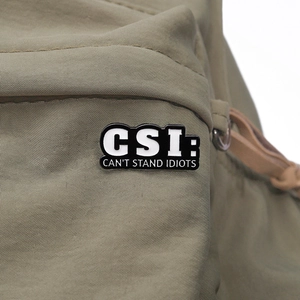 Detail of CSI: CAN'T STAND IDIOTS enamel pin on a green nylon backpack texture