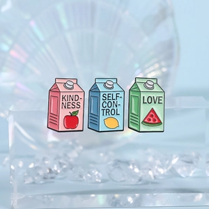 Three colorful cartoon milk carton enamel pins featuring fruit motifs on a clear stand