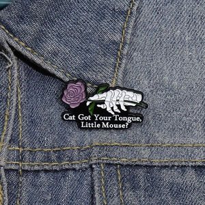 Detail of skull hand holding a purple rose enamel pin on blue denim fabric background