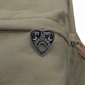 Macro shot of heart-shaped black enamel brooch with So Long and Goodnight text on backpack