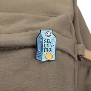 Detail of blue milk carton enamel pin with lemon and Self-Control text on canvas