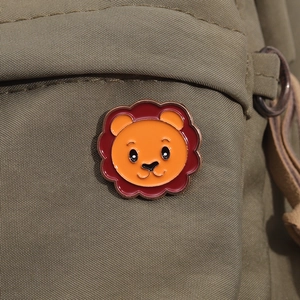 Detailed close-up of a cute cartoon lion enamel brooch on a green canvas bag