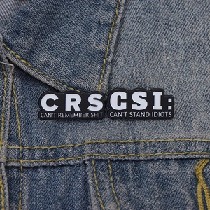 Macro shot of black enamel CSI and CRS pins on denim jacket showing fine craftsmanship