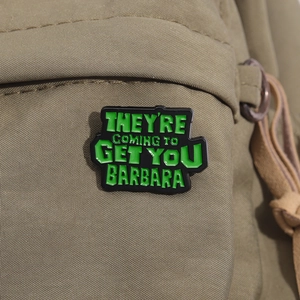 Détail d'une broche en émail vert sur sac à dos avec texte de citation de film d'horreur