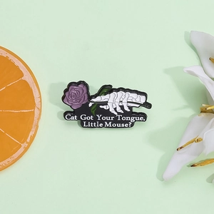 Gothic enamel pin featuring a skeleton hand holding a purple rose with text on green backdrop