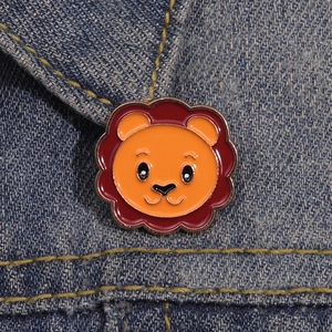 Cartoon lion enamel brooch pin in orange and red with golden trim on denim fabric