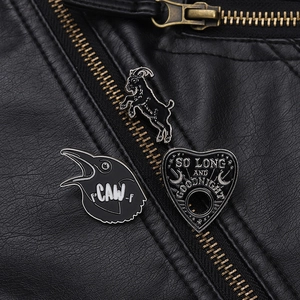 Detailed view of goat, crow, and heart enamel pins on a black leather jacket