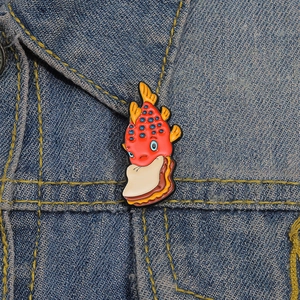 Gros plan d'un pin's en émail poisson mangeant un sandwich sur une veste en jean