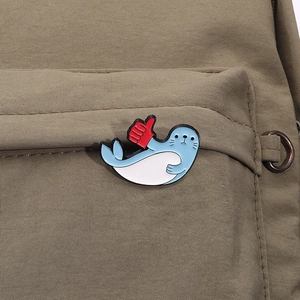 Detailed close-up of a cartoon seal enamel pin giving a thumbs up on green fabric
