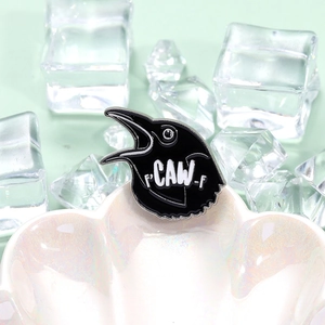 Whimsical black crow enamel brooch with F CAW F text on a stylish shell dish