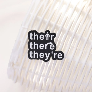 Minimalist enamel grammar badge featuring 'Their, There, They're' on black metal