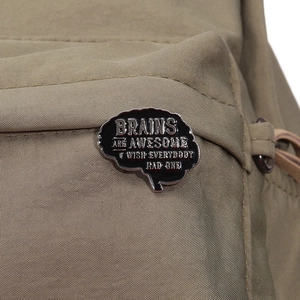 Close-up of a black enamel brain pin with white text on a khaki fabric backpack
