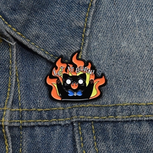 Creative black cat in flames enamel pin badge with Let It Burn text on denim fabric