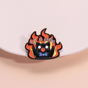 Cartoon black cat enamel pin with flames and LET IT BURN slogan on pink display stand