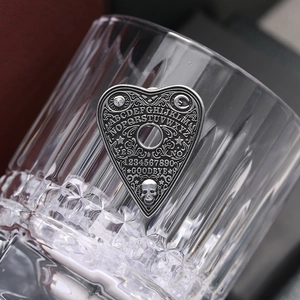 Vue macro d'une broche Ouija en métal en forme de cœur avec gravures gothiques sur un verre