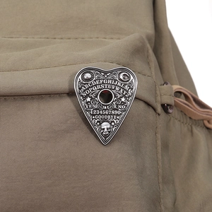 Close-up of heart-shaped Ouija Board enamel pin with gothic skull detail on canvas bag