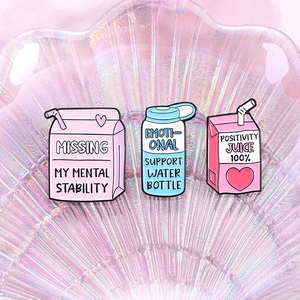 Three enamel pins with emotional quotes displayed on a pink iridescent shell tray