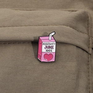 Détail du pin's émaillé rose Positivity Juice fixé sur un tissu en toile marron