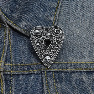 Vintage silver Ouija board enamel pin with skull motif on blue denim jacket