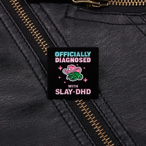 Détail macro du pin's émaillé grenouille avec texte Slay-DHD sur une veste en cuir