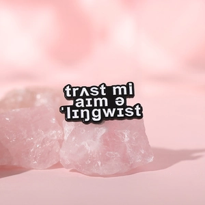 Black enamel pin with phonetic Trust me I'm a linguist text on soft pink background