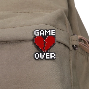 Macro detail of Game Over pixelated heart enamel pin attached to a canvas bag fabric