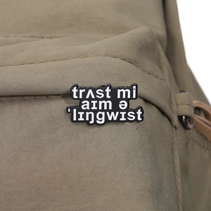 Detailed view of a black enamel pin with white linguistic text on a canvas bag