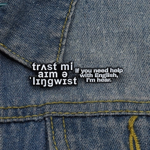 Detail of black enamel linguist quote badges pinned on a blue denim jacket texture