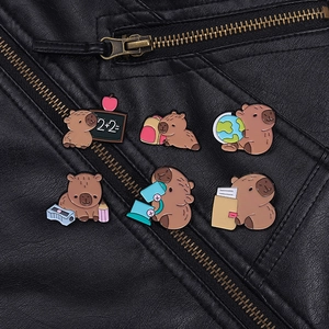 Detail of six capybara enamel pins with school and science themes on a black leather jacket