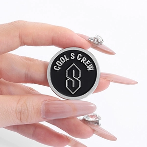 Minimalist round black and silver brooch with COOL S CREW lettering and geometric logo